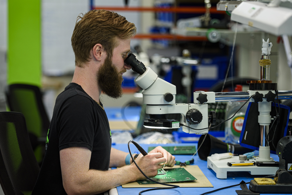 A product engineer working on a circuit board, looking through a microscope