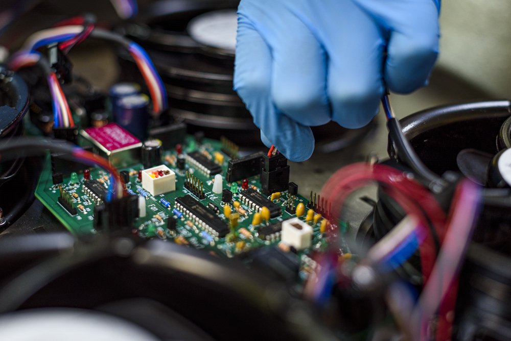 A circuit board being worked on by someone wearing blue vinyl gloves